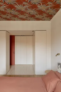 A bright and inviting bedroom with a red door, white walls, and a bed positioned towards the right side of the room