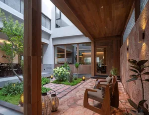 Open living room with a wooden floor, natural light, and modern furniture, including a couch, chair, and dining table, with a potted plant adding greenery