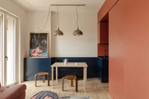A well-lit living room with a wooden floor, a dining table, chairs, a couch, and a painting on the wall, creating a warm and cozy atmosphere