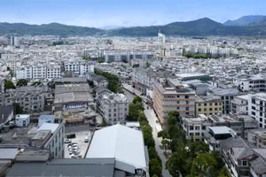 A bustling city with various buildings, including apartment buildings and a hotel, made of concrete, steel, and glass, with a busy street and natural lighting