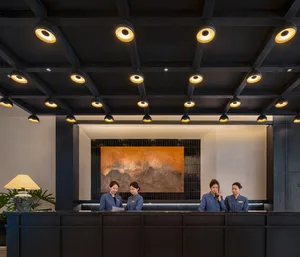 A bright and welcoming hotel lobby with a modern style, featuring a large painting, potted plants, a couch, and a chair, lit by bright lighting
