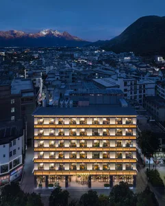 一座高聳飯店建築，擁有黃色木質立面，背後是城市天際線，其他建築與傍晚燈光