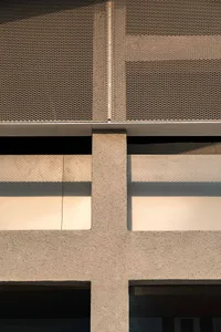 Grey concrete building with a metal fence attached to the wall, set against a bright and open background