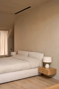 Cozy bedroom with a white bed, tan comforter, wooden nightstand, and natural light from an open window