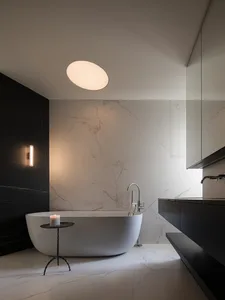 A modern bathroom with a white bathtub, sink, and mirror, featuring a round light fixture and a clean, minimalist aesthetic