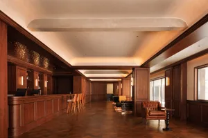 A modern lounge area with wooden floors and walls, featuring a bar, chairs, a couch, and a dining table, with a warm and inviting atmosphere