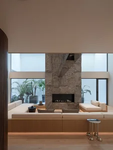 Cozy living room with a stone fireplace, wood furniture, and a potted plant, featuring natural light and a warm atmosphere