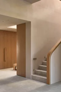 A wooden staircase in a cozy home with a white color, located in a hallway with a doorway at the bottom of the stairs