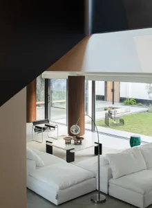 A well-lit living room with a large window, a white couch, a chair, and a dining table, giving a clean and minimalist appearance