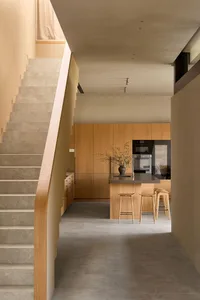 A modern kitchen with wooden floors and cabinets, featuring a sink, microwave, and refrigerator, with two chairs and bright, warm lighting