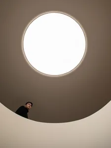 A man stands under a large round white light fixture in a modern minimalist room with a circular design and clean aesthetic