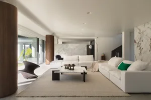 A modern living room with a white couch, chair, and coffee table, surrounded by various decorative items and natural light from the windows