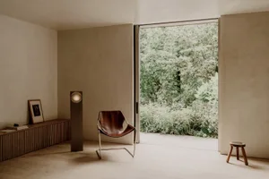 Cozy living room with a brown leather chair, lamp, and natural light from a large window, decorated with potted plants