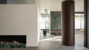 A modern living room with a predominantly white color scheme, a stone wall, a fireplace, and a potted plant, well-lit by natural light through the windows
