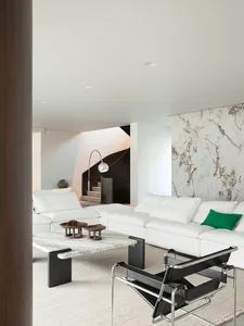Comfortable living space with a white couch, chair, and coffee table, featuring a large window and natural light, decorated with a vase and bowl