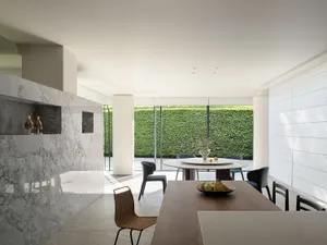 A modern kitchen with a wooden dining table and chairs set with a bowl of fruit, illuminated by natural light