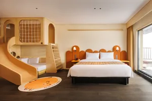 Cozy bedroom with a bed, chair, and desk, surrounded by white walls and natural light