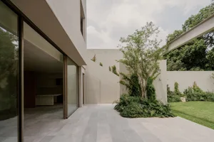 A modern house with a concrete exterior, a large glass door, and a staircase leading to the second floor, surrounded by a tree in the front yard