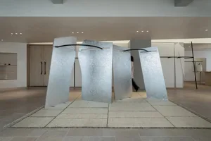 A contemporary gallery space with a large metal sculpture as the main attraction, surrounded by soft and diffused lighting