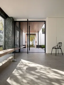 Bright and welcoming open living space with marble flooring, a black chair, a bench, and a dining table, filled with natural light