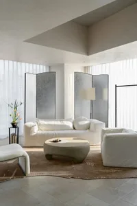 Well-lit modern living space with a white couch, chair, and coffee table, surrounded by natural light from windows