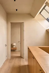 A calm and inviting bedroom with a wooden floor, a white wall, and natural light from a window