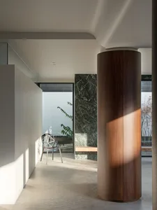 Cozy living room with a wooden floor, a white wall, a dining table, a chair, potted plants, a bench, and a vase, lit by natural light