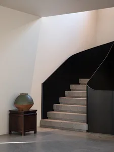 A residential staircase with a stone staircase and a clay vase on a table at the bottom, set in a warm and inviting space with natural lighting
