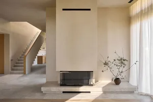 Cozy living room with a white fireplace, a couch, a potted plant, and a vase, well-lit by natural light from a window