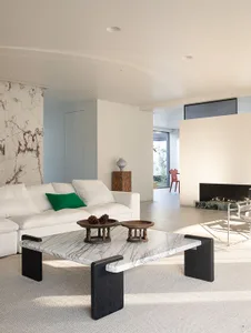 A modern living room with a white couch, a marble coffee table, and a fireplace, featuring a clean and inviting atmosphere with natural light and a cozy fireplace