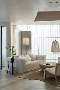 A modern living room with a white couch, chair, and potted plant, filled with natural light and a warm atmosphere