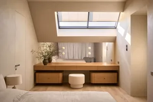 Cozy bedroom with a bed, chair, and dining table, featuring wood and glass materials, with natural light streaming in through the large window