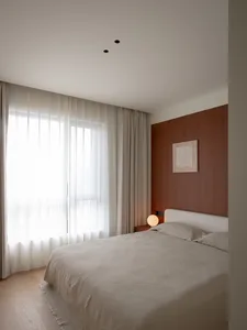 Cozy modern bedroom with a wooden floor, a bed against the wall, a window, and a floor lamp, well-lit and inviting