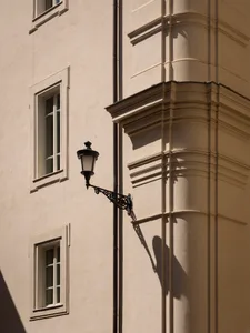 A stone building with a metal light fixture attached to its side, illuminated by the light, creating a shadow on the building's surface