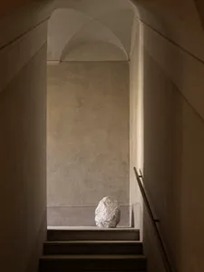 A traditional hallway with a stone staircase, stone wall, and stone column, set in a dimly lit space with a moody atmosphere