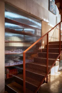 A modern staircase in a kitchen area with a metal railing and brown color scheme, surrounded by a pantry and natural light