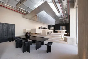 Modern open-concept living space with a black dining table, black and white chairs, a kitchen area, and natural light from windows