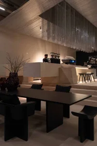 A modern restaurant interior with a dining area and bar, featuring wood and stone materials, natural lighting, and a relaxed atmosphere