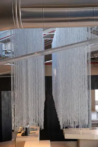A dimly lit room with a black and white color scheme, featuring numerous chains hanging from the ceiling at various heights and angles, creating a modern and minimalistic atmosphere