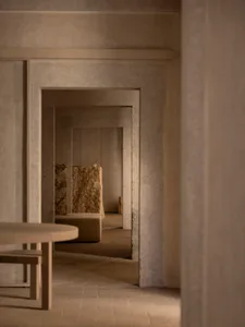 A large, open space with a stone floor, a stone table, and two benches, featuring a mirror on the wall and an elegant atmosphere