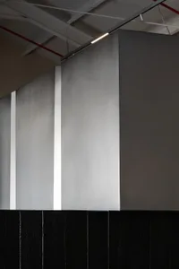 A calm and minimalistic living space with a white wall and a black border, possibly a door or window frame, in a room with a couch in the background