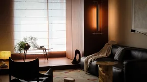 Comfortable living space with a black couch, a chair, and a dining table, set against a hardwood floor and a window, with soft natural light