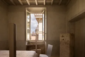 A calm and inviting bedroom with a white color scheme, a bed near the center, a chair by the window, and natural light from the window providing a view of the city