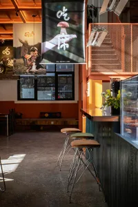 A cozy restaurant bar with a wooden counter and chairs, set in an Asian-inspired interior with inviting atmosphere
