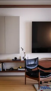 Cozy modern living room with a wooden floor, a flat screen TV, and a chair, surrounded by books and a lived-in atmosphere