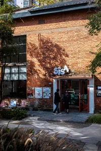 A casual restaurant with a brick facade, people walking in and out, and a chair in the foreground