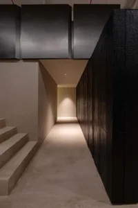 A dimly lit hallway with a concrete floor, metal railing, and a doorway leading to a room with a yellow wall