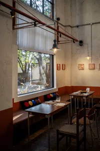 Bright and inviting restaurant interior with a long dining table, bar counter, and comfortable furniture, featuring white walls and natural light from windows