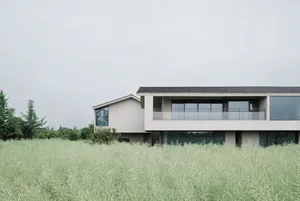 Large modern house with white exterior, surrounded by a lush green field, featuring a deck and balcony with natural light and warm ambiance