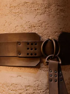 A black and white photograph of a leather belt with a buckle hanging on a wall, part of a larger display